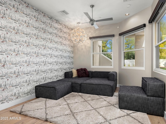 living area with visible vents, a healthy amount of sunlight, wood finished floors, baseboards, and wallpapered walls