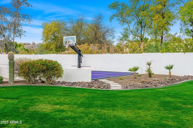 view of sport court featuring basketball hoop, a lawn, and fence