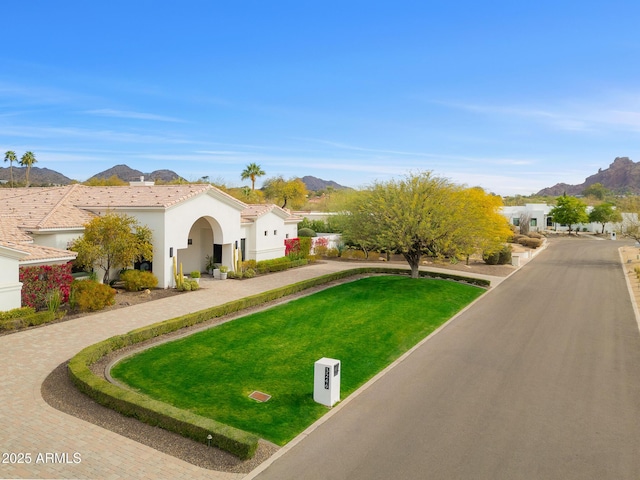 view of front of property featuring a mountain view, a front lawn, decorative driveway, and stucco siding