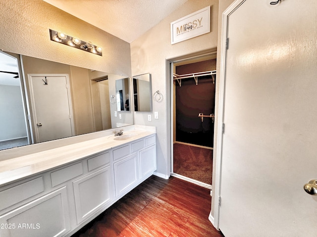 bathroom with wood finished floors, vanity, a textured ceiling, and a walk in closet
