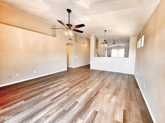 unfurnished living room with vaulted ceiling, arched walkways, a ceiling fan, wood finished floors, and baseboards