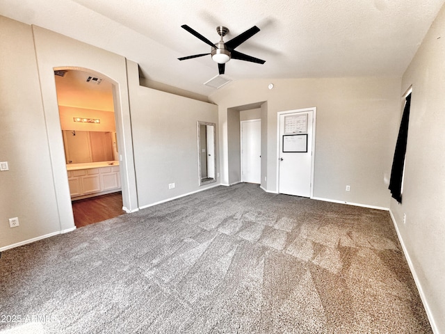 carpeted empty room with a ceiling fan, arched walkways, baseboards, and vaulted ceiling