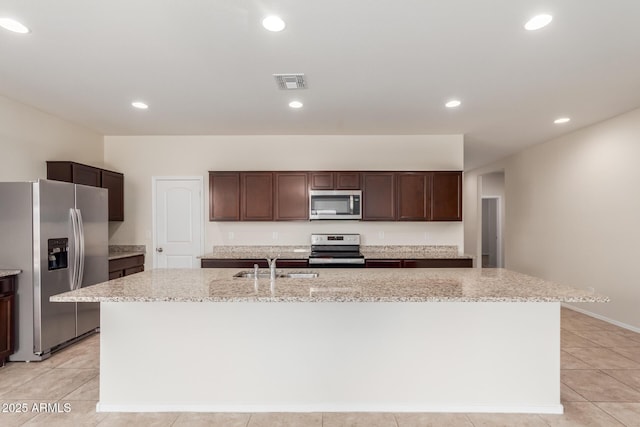 kitchen with light stone countertops, a kitchen island with sink, appliances with stainless steel finishes, and dark brown cabinets