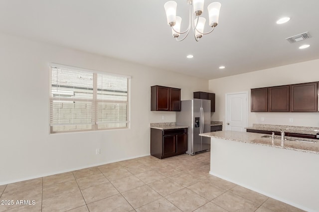 kitchen with sink, hanging light fixtures, stainless steel fridge, a notable chandelier, and light stone counters