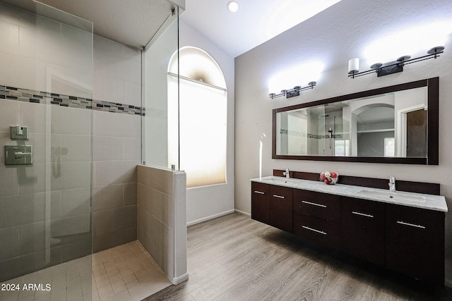 bathroom featuring hardwood / wood-style floors, tiled shower, double vanity, and vaulted ceiling