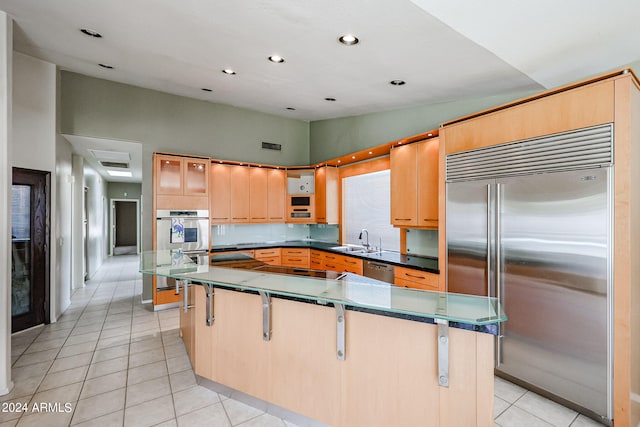 kitchen with stainless steel appliances, light tile patterned floors, a kitchen breakfast bar, sink, and a center island