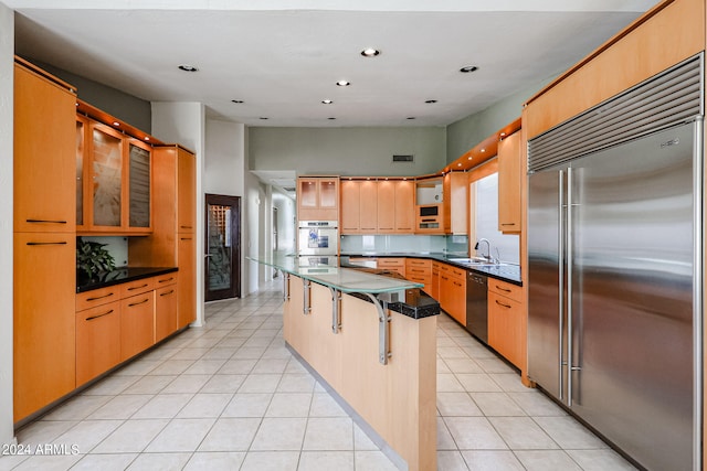 kitchen with a kitchen breakfast bar, light tile patterned flooring, appliances with stainless steel finishes, sink, and a kitchen island