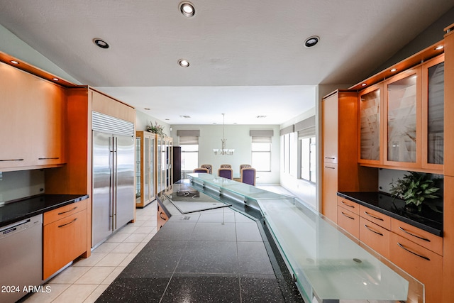 kitchen with hanging light fixtures, stainless steel built in refrigerator, white dishwasher, light tile patterned floors, and black electric stovetop