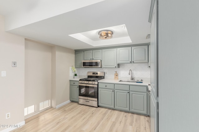 kitchen with a sink, light countertops, appliances with stainless steel finishes, backsplash, and a raised ceiling