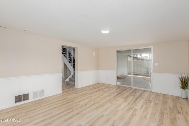 unfurnished room with light wood-style flooring, wainscoting, and visible vents