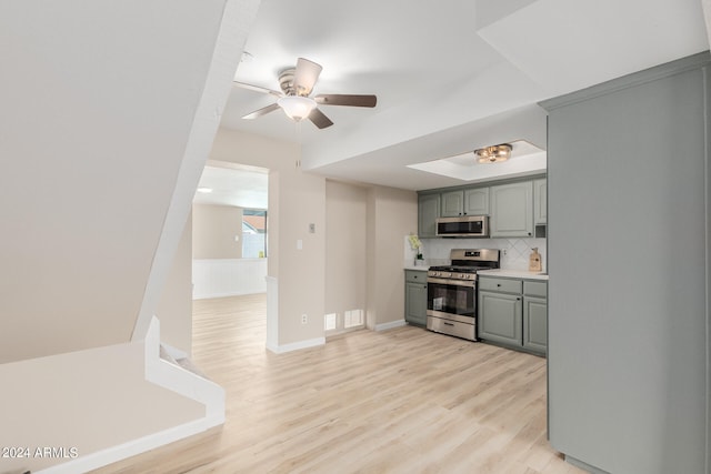 kitchen featuring light wood finished floors, stainless steel appliances, gray cabinets, light countertops, and backsplash