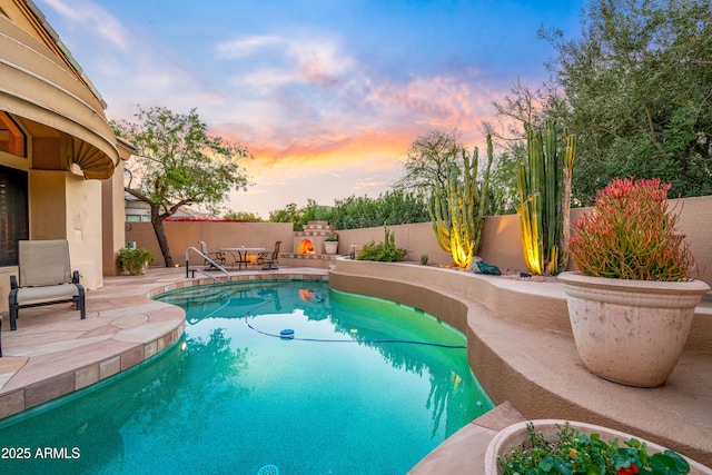 pool at dusk featuring a patio area, a fenced backyard, an outdoor fireplace, and a fenced in pool