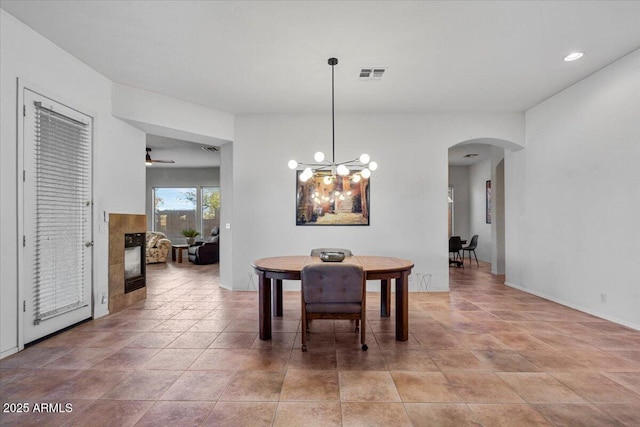 dining room with ceiling fan with notable chandelier and a tiled fireplace