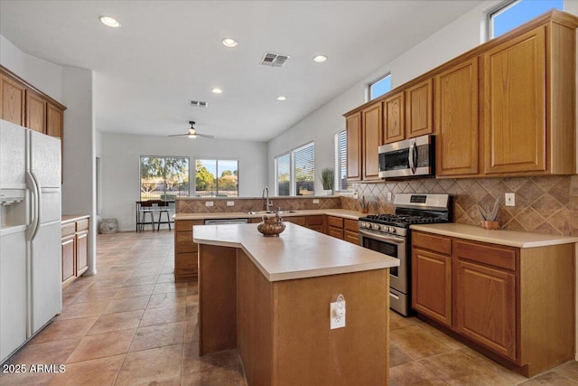 kitchen with ceiling fan, a center island, kitchen peninsula, decorative backsplash, and appliances with stainless steel finishes