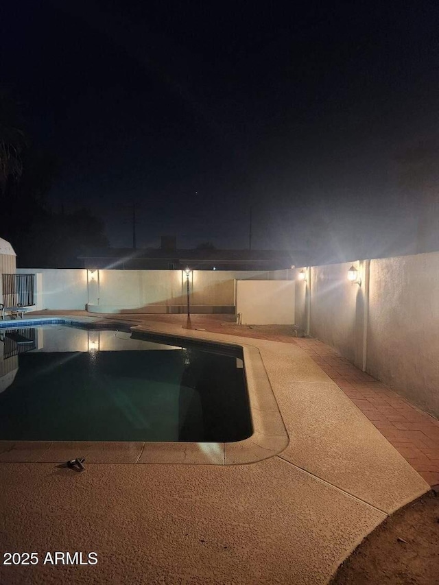 pool at night featuring a patio