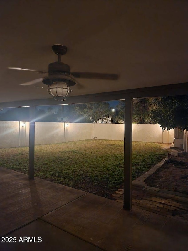 patio at night with ceiling fan and a yard