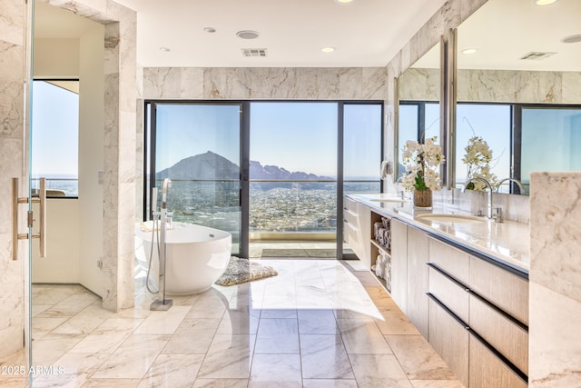 full bath with visible vents, marble finish floor, a freestanding tub, and a sink