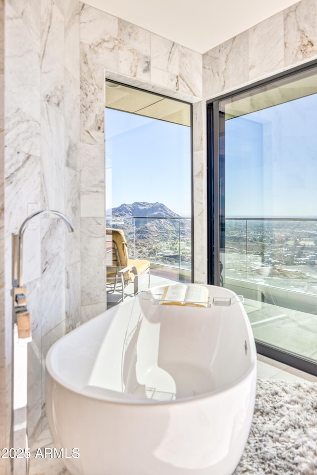 bathroom featuring a mountain view, a freestanding bath, and tile walls