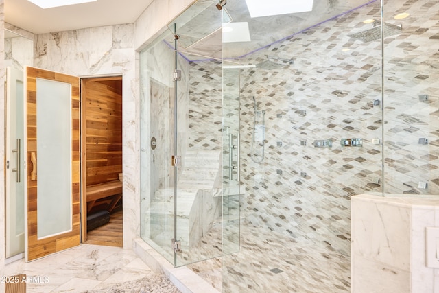 bathroom with marble finish floor, a skylight, and a shower stall