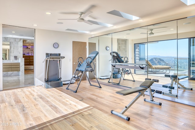 workout area featuring a ceiling fan, wood finished floors, recessed lighting, a mountain view, and a skylight