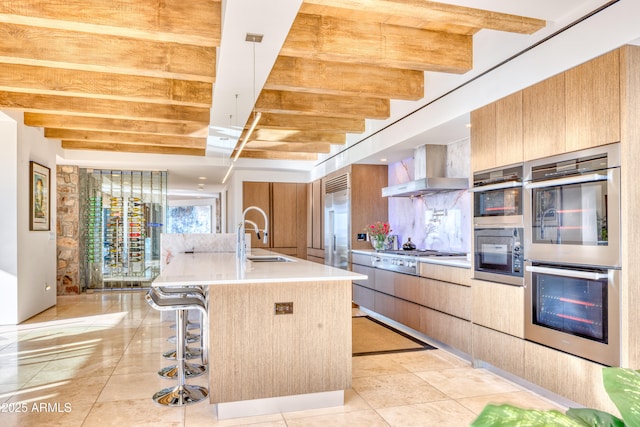 kitchen featuring a center island with sink, stainless steel appliances, modern cabinets, wall chimney exhaust hood, and a sink