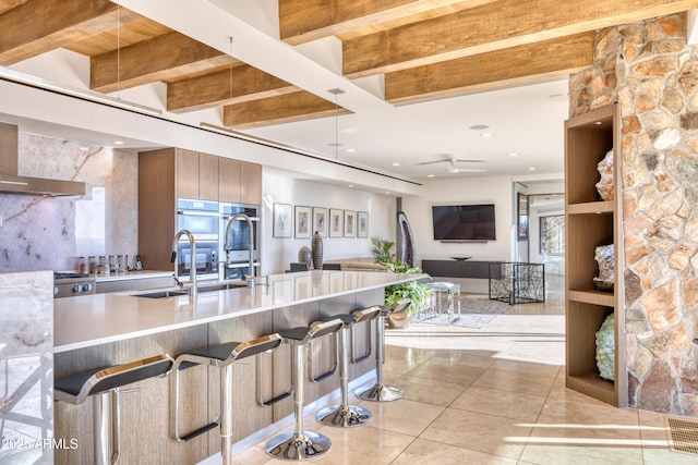 kitchen with modern cabinets, a sink, double oven, a breakfast bar area, and light countertops