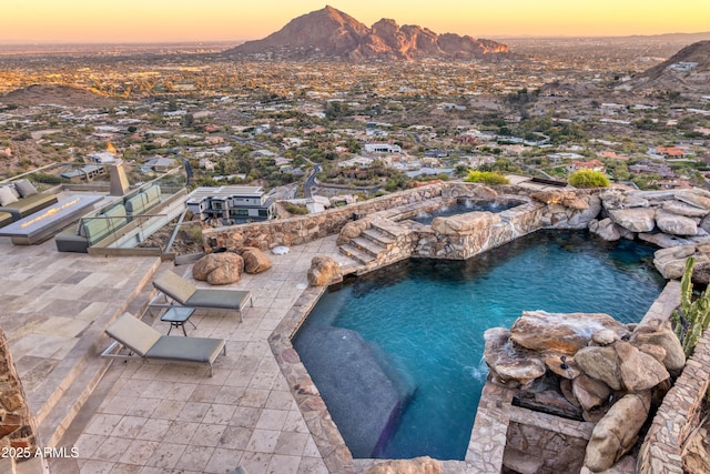 pool at dusk featuring a patio area, an outdoor pool, a mountain view, and an in ground hot tub