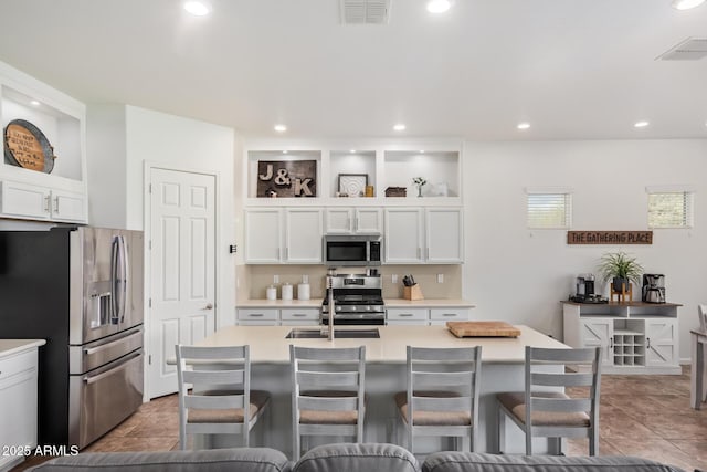 kitchen with white cabinetry, a kitchen bar, stainless steel appliances, and a center island with sink