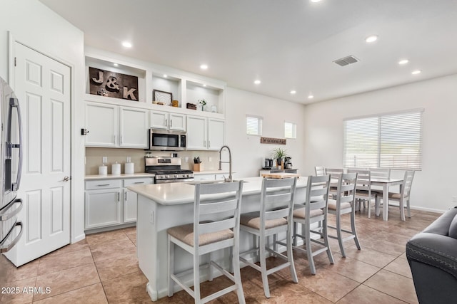 kitchen featuring white cabinetry, appliances with stainless steel finishes, a kitchen island with sink, and light tile patterned floors