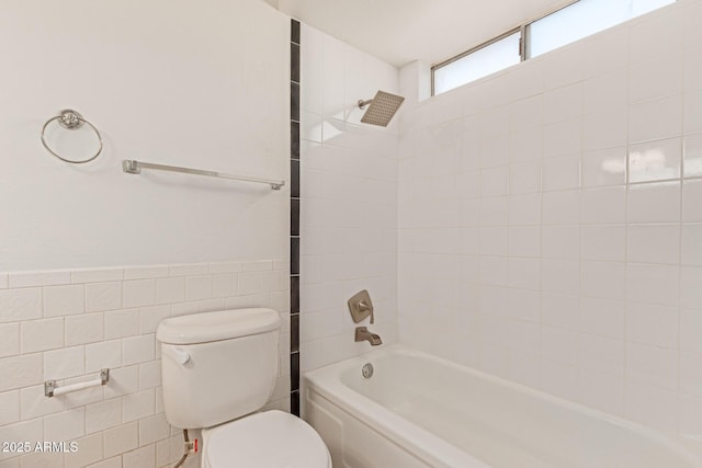 bathroom featuring tiled shower / bath combo, toilet, and tile walls