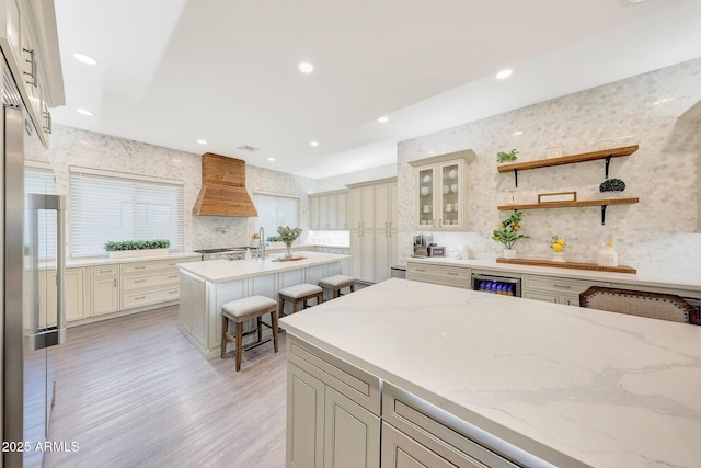 kitchen featuring cream cabinetry, custom range hood, a breakfast bar, and an island with sink