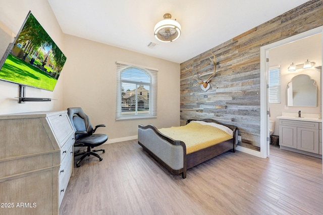 bedroom featuring wooden walls, connected bathroom, sink, and light wood-type flooring