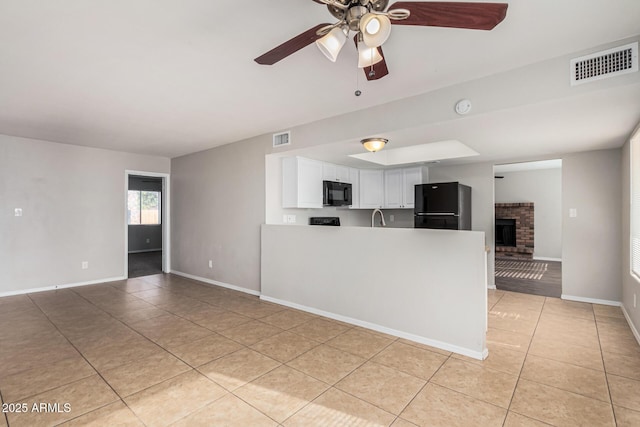 kitchen with white cabinetry, ceiling fan, a fireplace, light tile patterned flooring, and black appliances