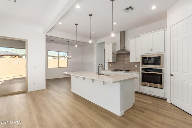 kitchen with an island with sink, white cabinetry, sink, wall chimney exhaust hood, and stainless steel appliances