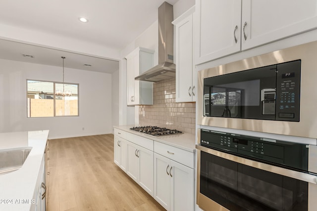 kitchen featuring wall chimney exhaust hood, white cabinets, decorative light fixtures, and stainless steel appliances