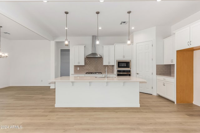 kitchen with a kitchen island with sink, stainless steel oven, wall chimney range hood, black microwave, and light hardwood / wood-style floors