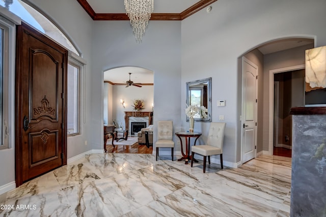 foyer entrance featuring ceiling fan with notable chandelier, light hardwood / wood-style floors, a high end fireplace, and ornamental molding