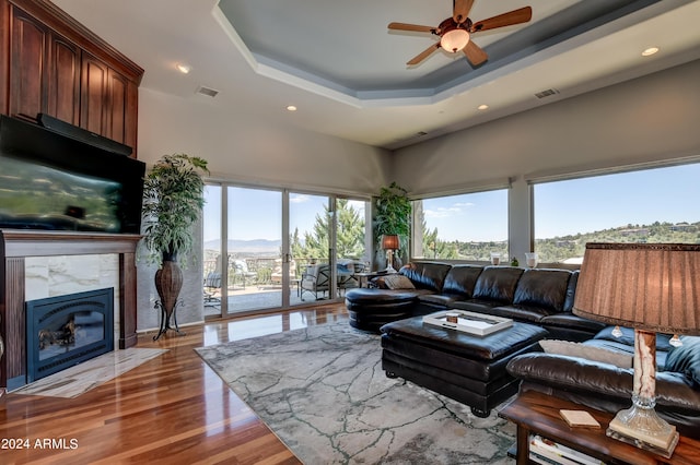 living room featuring hardwood / wood-style floors, a raised ceiling, a high end fireplace, and ceiling fan