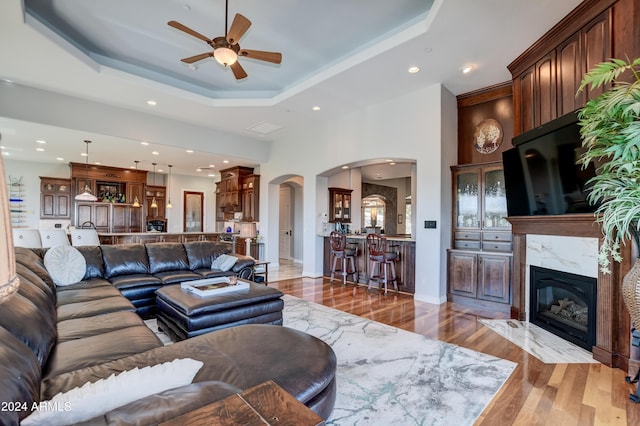 living room featuring a raised ceiling, light hardwood / wood-style flooring, ceiling fan, and a high end fireplace