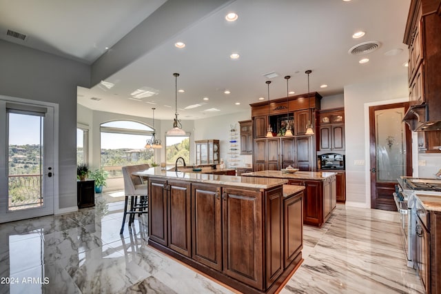 kitchen with a large island with sink, light stone counters, high end stainless steel range, light tile patterned floors, and hanging light fixtures