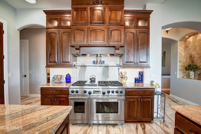 kitchen with wall chimney exhaust hood, tasteful backsplash, double oven range, and light stone countertops