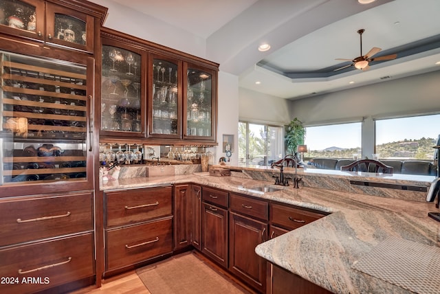 bar with sink, wine cooler, light stone countertops, a tray ceiling, and ceiling fan
