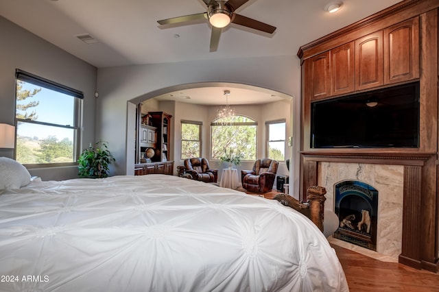 bedroom with multiple windows, a fireplace, ceiling fan with notable chandelier, and hardwood / wood-style floors