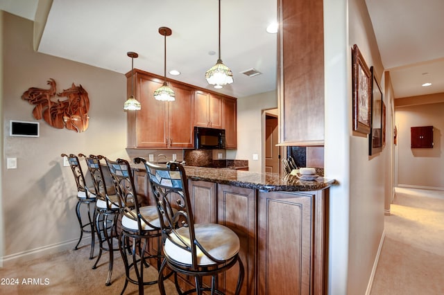kitchen with light colored carpet, hanging light fixtures, kitchen peninsula, dark stone countertops, and a breakfast bar area