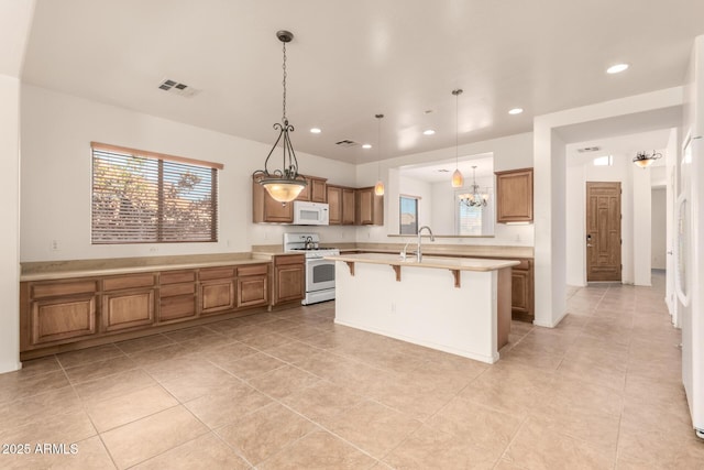 kitchen featuring an island with sink, a kitchen bar, hanging light fixtures, and white appliances