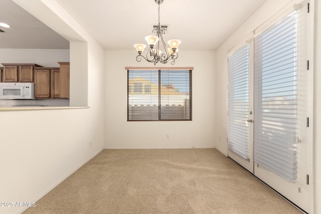 unfurnished dining area featuring a chandelier and light colored carpet