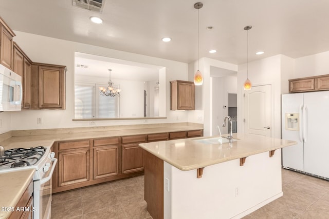 kitchen featuring a notable chandelier, a center island with sink, a breakfast bar, sink, and white appliances