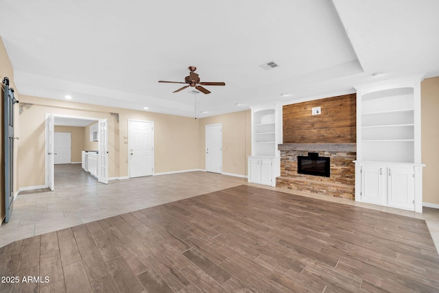 unfurnished living room featuring built in shelves, a fireplace, a barn door, and ceiling fan