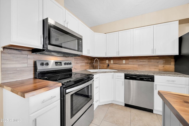 kitchen featuring butcher block countertops, sink, light tile patterned floors, stainless steel appliances, and white cabinets