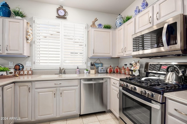 kitchen featuring a sink, stainless steel appliances, light tile patterned floors, light countertops, and white cabinets